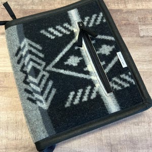 May include: Black and white patterned laptop sleeve with a zippered pocket and a black strap. The sleeve has the text "Lariat Case" on the side.