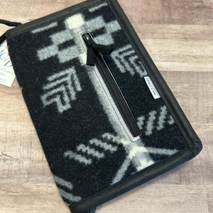 May include: Black and white patterned wallet with a zippered pocket and a black strap. The wallet is made of a soft, fuzzy material and has a "Great Lakes" label.
