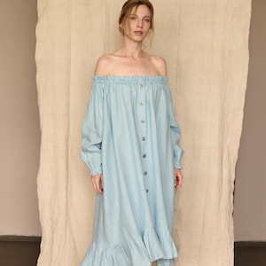 Puede incluir: Vestido azul claro con hombros descubiertos, mangas largas y botones delanteros. El vestido presenta un escote y un dobladillo con volantes, y se lleva con sandalias color crema. El vestido está hecho de una tela suave y fluida.