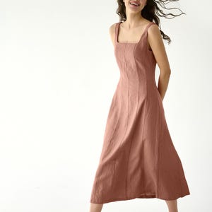 Puede incluir: Vestido midi rosa empolvado con escote cuadrado y tirantes finos. El vestido tiene costuras verticales y una falda acampanada. La modelo lleva sandalias de tacón negras. El vestido está hecho de una tela suave y fluida.