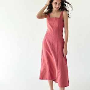 Puede incluir: Vestido sin mangas, largo midi, en color rosa empolvado. El vestido presenta un escote cuadrado y costuras verticales en la parte delantera. La modelo lleva sandalias negras. El vestido está hecho de tejido ligero.