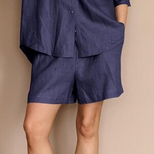 Puede incluir: Conjunto de shorts de lino azul marino. Los shorts tienen bolsillos y se combinan con una camisa abotonada a juego. La tela parece ligera y adecuada para el clima cálido.