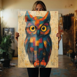 Könnte beinhalten: Ein farbenfrohes Eulen-Gemälde mit einem lebendigen Design. Die Eule weist orange, blaue und gelbe Farbtöne mit einem geometrischen Muster auf. Das Kunstwerk wird auf einem strukturierten, hellfarbigen Hintergrund präsentiert, was einen auffälligen visuellen Effekt erzeugt.