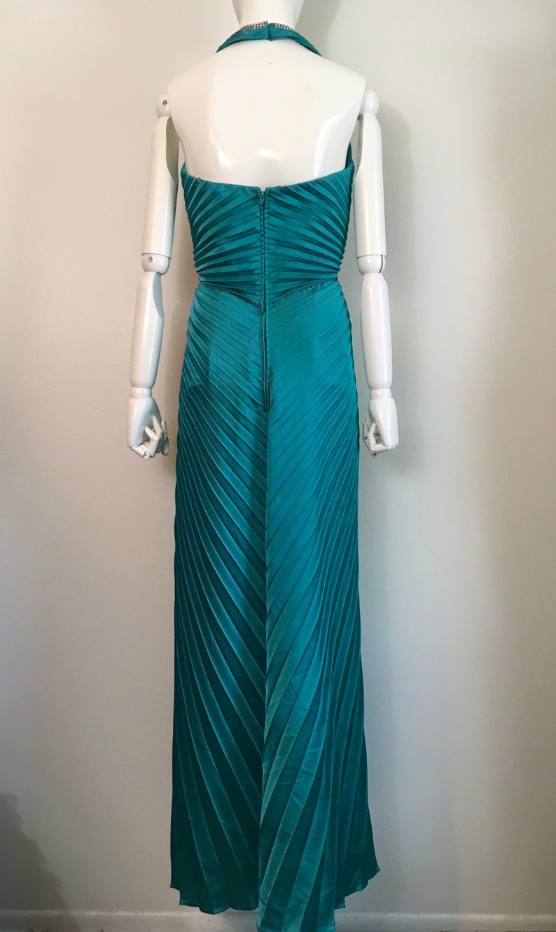 May include: Teal blue halter-style maxi dress with a pleated skirt and a zip closure at the back.