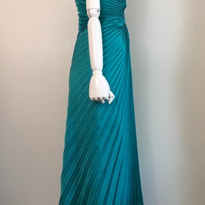 May include: A teal blue halter-style maxi dress with a pleated skirt. The dress is made of a soft, flowing fabric and has a flattering fit.