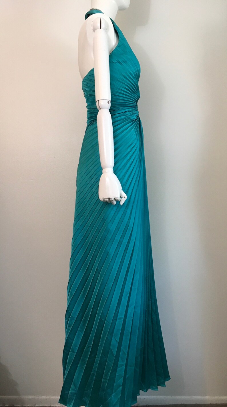 May include: A teal blue halter-style maxi dress with a pleated skirt. The dress is made of a soft, flowing fabric and has a flattering fit.