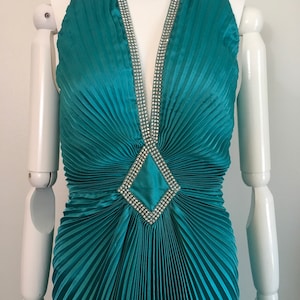 May include: Teal blue halter dress with a pleated skirt and a diamond-shaped rhinestone embellishment at the neckline.