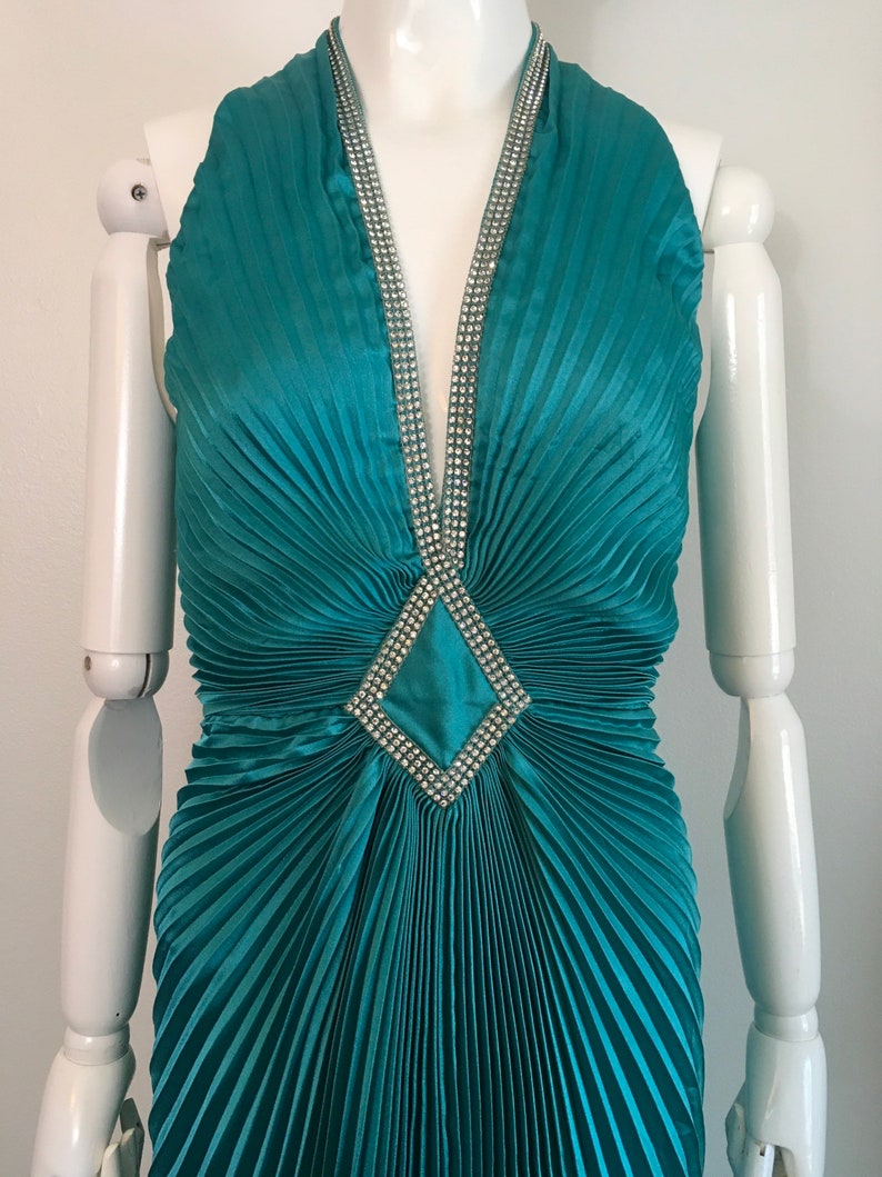May include: Teal blue halter dress with a pleated skirt and a diamond-shaped rhinestone embellishment at the neckline.