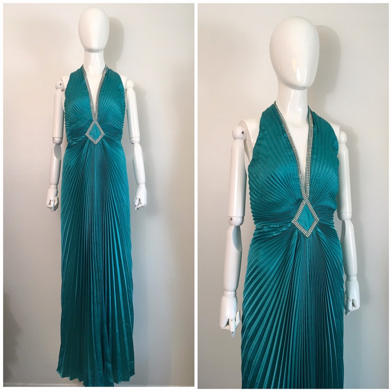 May include: A teal blue halter-style evening gown with a pleated skirt and a diamond-shaped embellishment at the neckline.