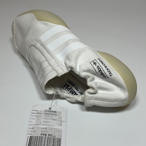 May include: White Adidas Taekwondo W shoes with three stripes on the side. The shoe has a rounded toe and a tag that says "PRE SELL". The shoe is designed for martial arts.
