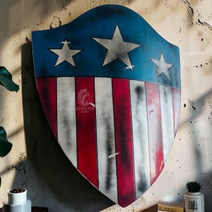 May include: A shield with a blue top section featuring three white stars and a red and white striped bottom. The shield is mounted on a textured wall. The shield has a distressed, vintage appearance.