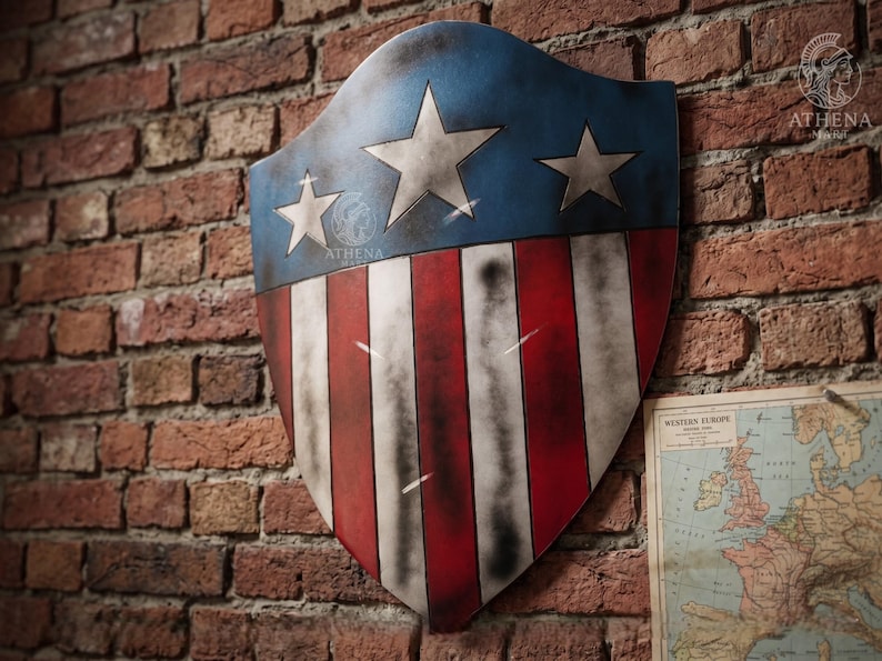 May include: A shield with a blue top section featuring three white stars and a red and white striped lower section. The shield is mounted on a brick wall. The shield has a distressed, aged appearance.