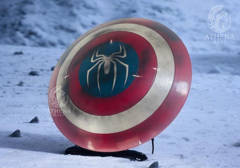 Puede incluir: Un escudo rojo, blanco y azul con un emblema de ara&ntilde;a plateada sobre un c&iacute;rculo azul. El escudo tiene un aspecto envejecido y se muestra sobre una superficie nevada. Es un accesorio o art&iacute;culo de colecci&oacute;n.