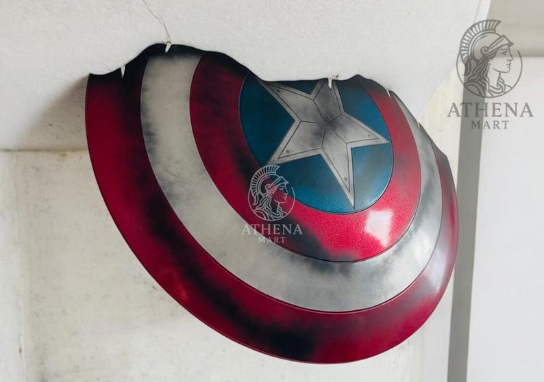 May include: A Captain America shield replica, featuring a red, white, and blue color scheme. The shield has a star in the center and is designed with a distressed, battle-worn appearance. The shield is a prop or collectible item.