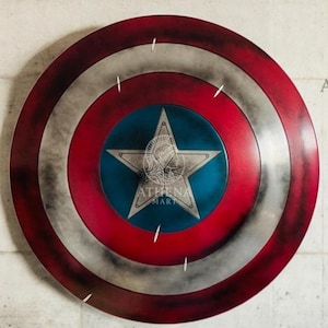 May include: A round shield with a red, white, and blue color scheme. The shield features a central blue circle with a white star, surrounded by red and white concentric rings. The shield has a distressed, weathered appearance, and the Athena Mart logo is visible.