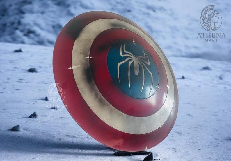 Puede incluir: Un escudo rojo, blanco y azul con un emblema de ara&ntilde;a plateada en el centro. El escudo tiene un aspecto desgastado y est&aacute; sobre un fondo nevado. Es un accesorio o art&iacute;culo de colecci&oacute;n.