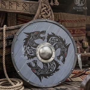 May include: A circular grey shield featuring a black wolf design and a silver metal centre. The shield has a silver metal rim and is decorated with rivets. The Athena Mart logo is visible on the shield.