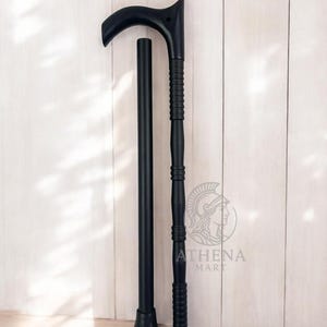 Könnte beinhalten: Schwarzer Gehstock mit gebogenem Griff und abnehmbarem Schaft. Der Stock hat einen strukturierten Griff und eine Gummispitze. Der Stock ist im zusammengebauten Zustand etwa 94 cm hoch.