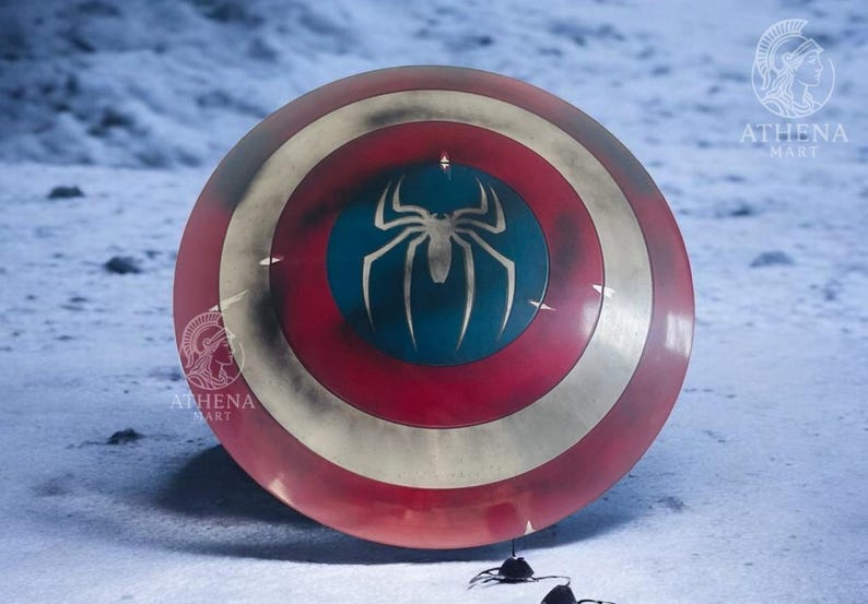 Puede incluir: Un escudo redondo con una combinaci&oacute;n de colores rojo, blanco y dorado. El centro presenta un c&iacute;rculo azul con un emblema de ara&ntilde;a blanco. El escudo es un accesorio o art&iacute;culo de colecci&oacute;n, probablemente inspirado en un tema de superh&eacute;roes.