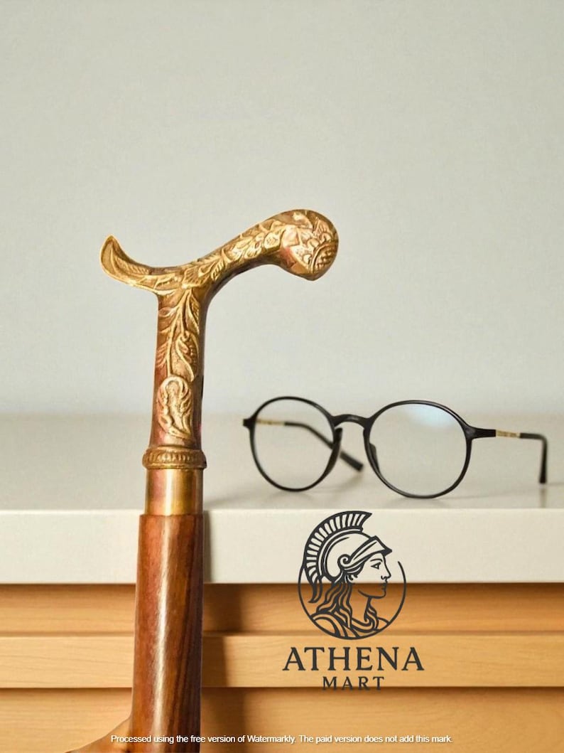 May include: A decorative walking cane with a detailed gold-colored handle and a wooden shaft. Round black eyeglasses rest on a white surface. The Athena Mart logo is visible.