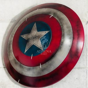 May include: A Captain America shield, featuring a red, white, and blue color scheme with a central blue star. The shield has a distressed, weathered appearance, with a silver star in the center. The shield is a replica of the iconic superhero prop.