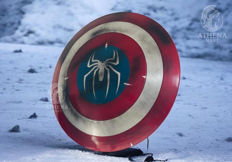 Puede incluir: Un escudo redondo con un dise&ntilde;o rojo, blanco y azul. El escudo presenta un centro azul con un emblema de ara&ntilde;a blanco. El escudo es un accesorio, probablemente para cosplay o exhibici&oacute;n.