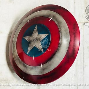 May include: A round shield with a red, white, and blue color scheme. The shield features a central blue circle with a white star and a silver border. The outer ring is red, with white and silver accents. The shield has a distressed, weathered appearance.