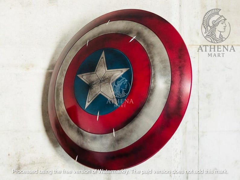 May include: A round shield with a red, white, and blue color scheme. The shield features a central blue circle with a white star and a silver border. The outer ring is red, with white and silver accents. The shield has a distressed, weathered appearance.