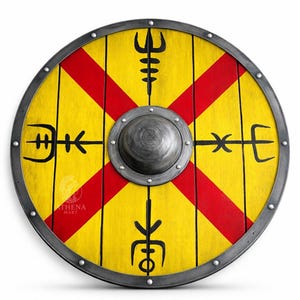May include: A circular Viking shield featuring a yellow base with a red cross pattern. It has a metal rim and a central boss. Black symbols are painted on the yellow surface. This shield is a decorative item.