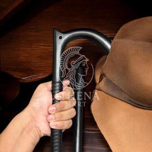 May include: A black walking cane with a curved handle and a textured grip. The cane has a logo that says "ATHENA MART" with a graphic of a woman's profile. A brown hat hangs on the cane.