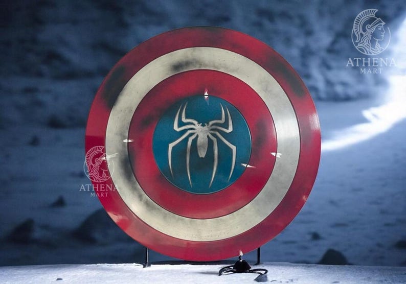 Puede incluir: Un escudo redondo con un dise&ntilde;o rojo, blanco y azul. El escudo presenta un gran emblema de ara&ntilde;a blanca sobre un centro azul. El escudo est&aacute; sostenido por un soporte negro. El escudo es un accesorio o art&iacute;culo de colecci&oacute;n.