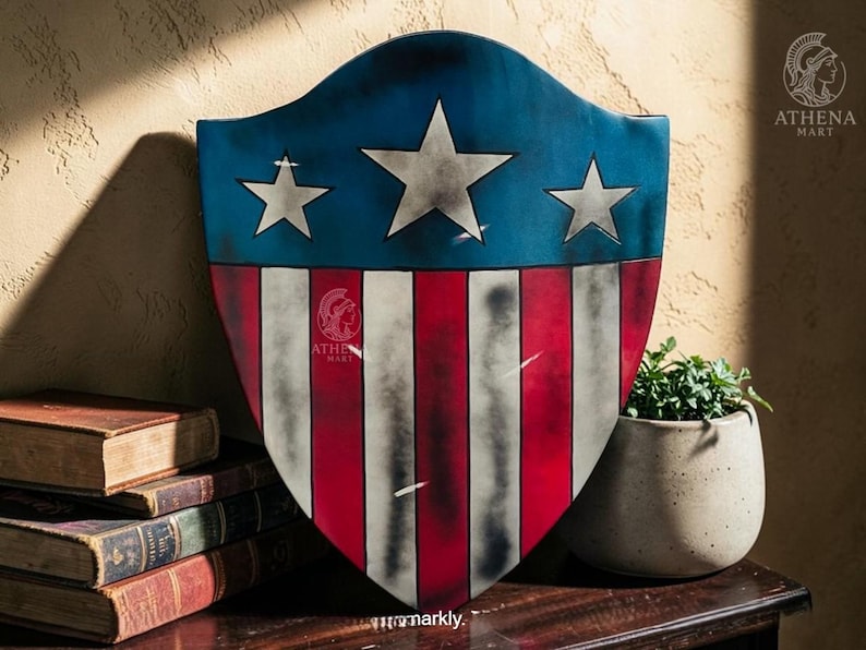 May include: A shield with a blue top section featuring three white stars, transitioning to red and white stripes. The shield has a distressed, vintage appearance. The Athena Mart logo is visible on the shield. A stack of old books and a potted plant are in the background.