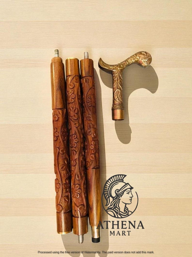 May include: A wooden walking cane with a decorative brass handle and three carved wooden sections. The handle features an ornate floral design. The cane sections are brown with carved floral patterns. The logo for Athena Mart is visible.