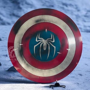 Puede incluir: Escudo redondo con una combinaci&oacute;n de colores rojo, blanco y azul. El escudo presenta un gran emblema de ara&ntilde;a blanca sobre un c&iacute;rculo azul en el centro. El escudo tiene una apariencia desgastada, lo que sugiere una est&eacute;tica desgastada por la batalla.