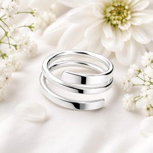 May include: A polished silver ring featuring a bypass design with two overlapping bands that wrap around the finger. The metal has a smooth, reflective surface with clean, rounded edges, creating a continuous spiral appearance in a bright silver tone.
