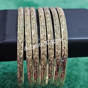 Puede incluir: Un conjunto de siete pulseras doradas con un dise&ntilde;o floral en relieve. Las pulseras est&aacute;n dispuestas una al lado de la otra, mostrando sus intrincados patrones. El texto "Accents4Copper" es visible.