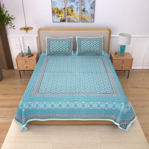 Puede incluir: Una colcha turquesa y dos fundas de almohada con un patrón geométrico. La colcha presenta un borde con diseños florales y geométricos en tonos azules, grises y blancos. La ropa de cama está sobre una estructura de cama de madera.
