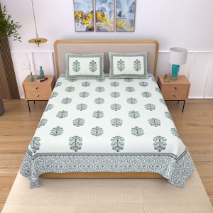Puede incluir: Juego de sábanas blancas con un estampado floral repetido en tonos verdes y azules. El juego incluye una sábana bajera, dos fundas de almohada y un borde decorativo. La cama tiene un marco de madera clara y dos mesitas de noche a juego.