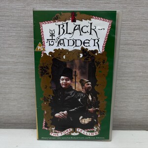 May include: A VHS tape of "The Black Adder: The Foretelling" with a green background. The cover features a gold ornate frame with two men in period clothing. The title is in a decorative font.