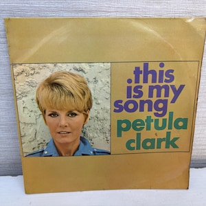 Peut inclure: Pochette de disque vinyle vintage avec Petula Clark. La couverture est beige avec une image rectangulaire de Clark en chemise bleue. Le texte indique ".this is my song" et "petula clark" en violet et vert.