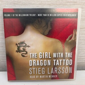 May include: Audiobook cover for "The Girl with the Dragon Tattoo" by Stieg Larsson. The cover features a person's back with a dragon tattoo. Text includes the title, author's name, and "Read by Martin Wenner."