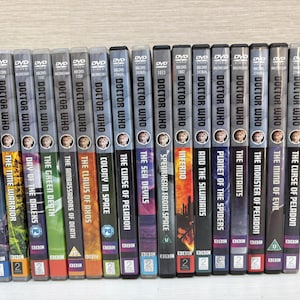 Puede incluir: Una colección de sets de DVD de Doctor Who, con títulos como "Death to the Daleks" y "The Time Warrior". Las portadas muestran títulos de episodios y retratos de personajes. Los DVD están en fila, con el logotipo de la BBC.