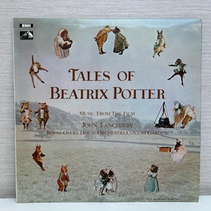 Può includere: Copertina di un album in vinile vintage per "Tales of Beatrix Potter". La copertina presenta illustrazioni dei personaggi della storia, con il titolo in grandi lettere marroni. Lo sfondo è un campo con una catena montuosa.