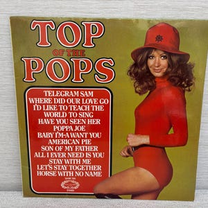 May include: A vintage "Top of the Pops" vinyl record album cover. The cover shows a woman in a red outfit and hat. The album title is in large red letters. Song titles are listed in a red box.
