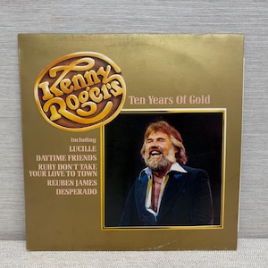 May include: A gold-toned album cover for Kenny Rogers' "Ten Years of Gold." The cover features a portrait of Kenny Rogers and the album title. The tracklist includes "Lucille," "Daytime Friends," and "Ruby Don't Take Your Love to Town."