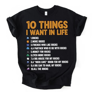 Pode incluir: Camiseta preta com o texto "10 THINGS I WANT IN LIFE" em laranja. A lista inclui desejos como rochas, amigos que gostam de rochas e uma caverna de rochas. Um design divertido e peculiar para os entusiastas de rochas.