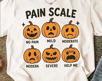 May include: White t-shirt with a "PAIN SCALE" graphic featuring six orange jack-o'-lanterns with varying expressions. The shirt includes the phrases "NO PAIN," "MILD," "MODERATE," "MODERA," "SEVERE," and "HELP ME."