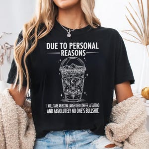 May include: Black t-shirt with white graphic text and a detailed iced coffee design. The text reads "DUE TO PERSONAL REASONS" above the coffee illustration, and "I WILL TAKE AN EXTRA LARGE ICED COFFEE, A TATTOO AND ABSOLUTELY NO ONE'S BULLSHIT" below.