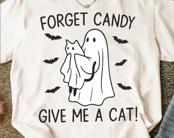 May include: Cream-colored t-shirt with a Halloween-themed graphic. The design features a ghost holding a cat, surrounded by bats, with the text "FORGET CANDY GIVE ME A CAT!" printed in black.