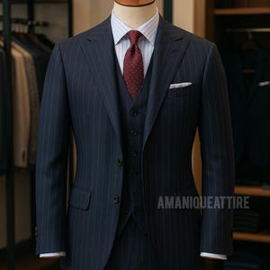 May include: A navy blue three-piece suit with subtle pinstripes, displayed on a mannequin. The suit includes a vest, jacket, and trousers, paired with a striped shirt and a burgundy dotted tie. A white pocket square adds a touch of elegance. The brand name "AMANIQUEATTIRE" is visible.